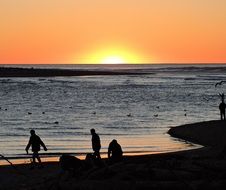 Silhouettes of the company of friends at the beautiful beach with colorful sunset on horizon