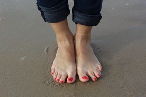 Feet with red pedicure on the beach on holiday