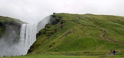 Beautiful waterfall on green hill under cloudy sky