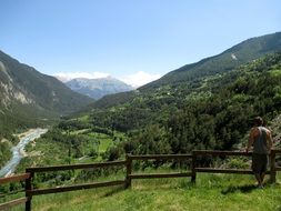 man stands near a fence on a background of green mountains