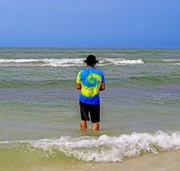young man in a yellow-blue t-shirt is fishing in the ocean
