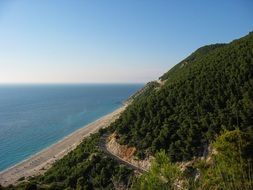 forested mountain side with road and beach at blue sea, Greece, Lefkada