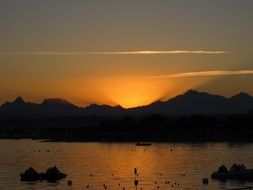 Sunset behind mountains at sea, orange sun beams on dusk sky, Egypt