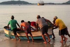 Team of Fishermen pushing Boat on sea