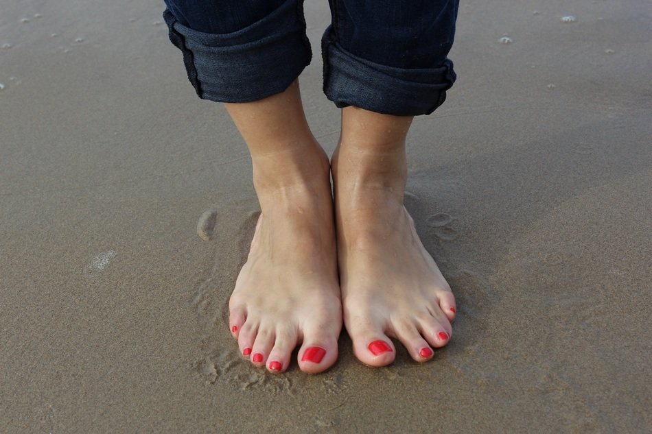 Feet with red pedicure on the beach on holiday