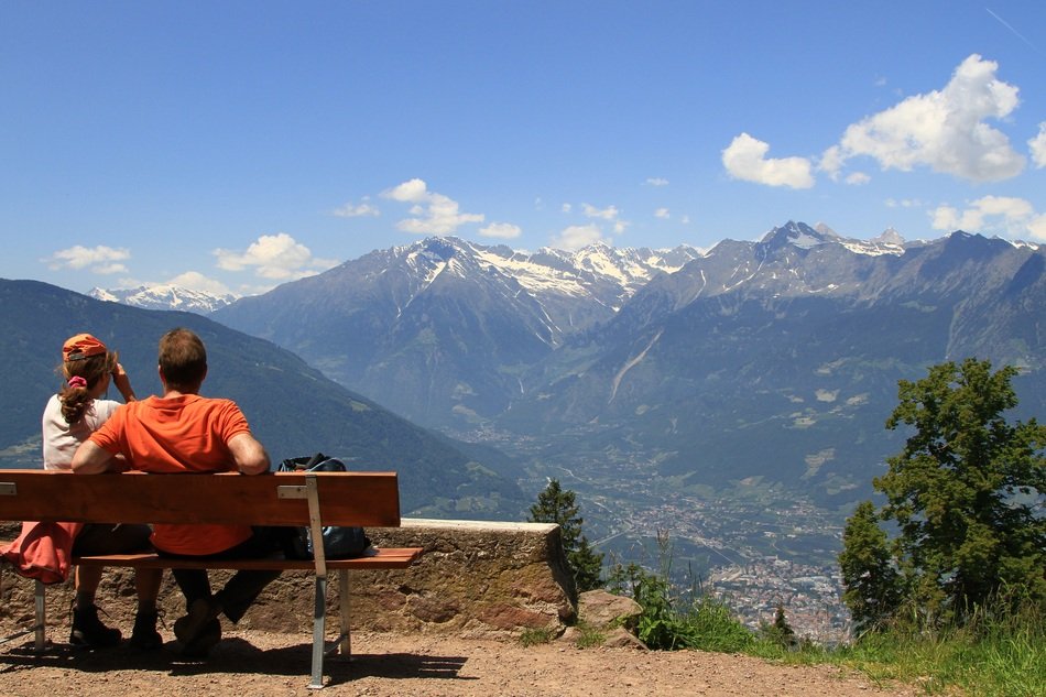 People on a bench admire a Meran city in a valley among the beautiful mountains in snow in Italy