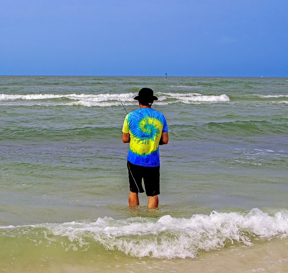 young man in a yellow-blue t-shirt is fishing in the ocean