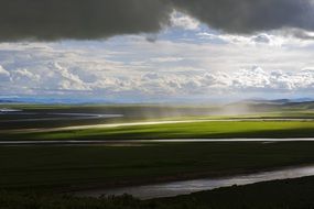 sunlight through dark clouds on green prairies