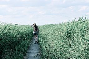 girl on a wooden path among tall grass