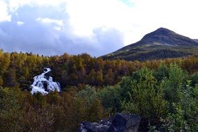 distant view of a waterfall in an autumn forest among the rocks
