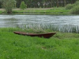 old wooden boat on the green bank of the river