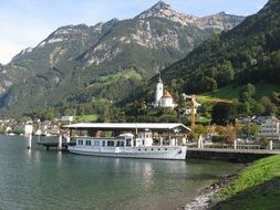 tourist boat at pier near old village in scenic mountains, switzerland