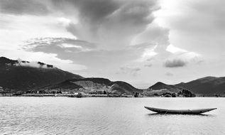 black and white photo of a boat on a lake near a mountain