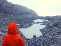 man in a bright jacket near a lake in the mountains of south america