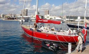 old man near red Sailboat at pier in view of city