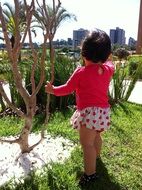 back view of Baby girl holding for branch at cityscape