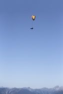 Paragliding, person on paraglider in blue sky above mountain summits