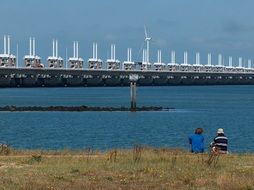 people sit on the shore of a huge bridge