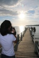 girl photographs sunrise from pier