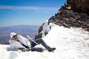 a man in a white jacket lies on a snowy mountain peak in Morocco