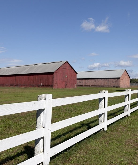 white wooden fence along large farm sheds on a sunny day