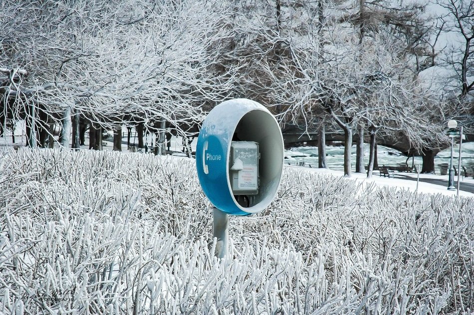 blue telephone box in the frozen grass against the background of a winter landscape