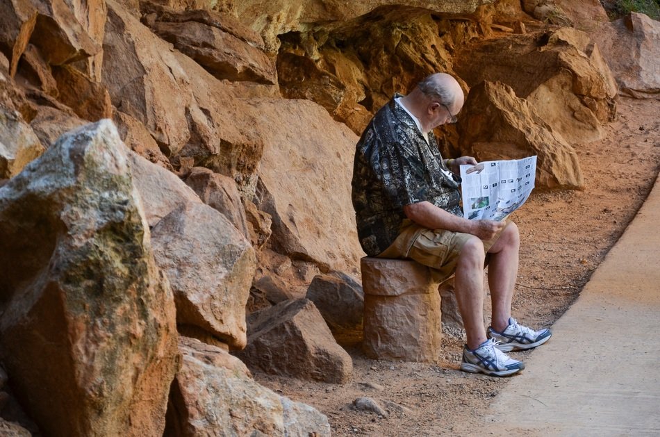 old man with paper sits on stone at red rock, Usa