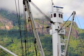 photo of masts of a cargo ship on a background of green mountains