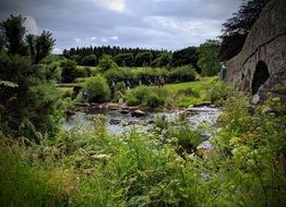 people at ancient stone bridge across small river in beautiful summer landscape, uk, england, cornwall