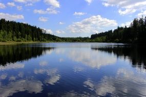 white clouds are reflected in the quiet surface of the lake