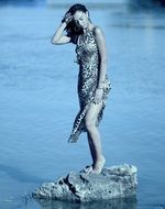brunette woman in a leopard dress on a stone among the the water in monochrome image