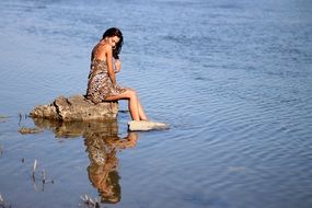 brunette woman in a leopard dress on a stone in the water