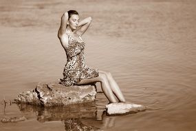 brunette in a leopard dress on a stone in the water in monochrome background
