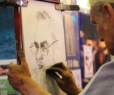 old artist drawing portrait of man in glasses with Charcoal