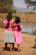back view of two child girls standing together in front of water, India, Karnataka