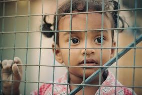 asian Child girl Looking through wire grid fence