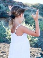 child girl in white dress with hands up outdoor, back view