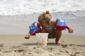 little girl plays with sand on the beach by the ocean