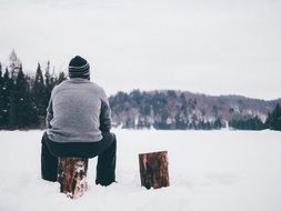 man sits on a log in a meadow in winter