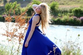 blonde in a long blue dress among nature