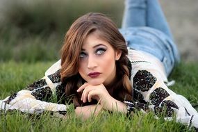 Portrait of a girl with make-up lying on the green grass