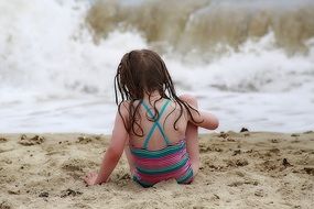 Child girl with wet hair sits on beach at Waves