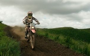 sports biker rides on a country road along a green field