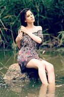 girl sits on a stone by the water