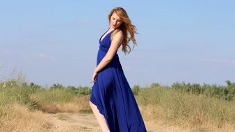 sensual girl in a long blue dress among nature on a sunny day
