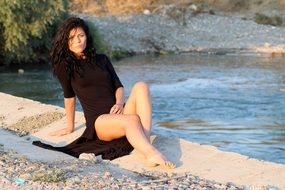 brunette in a black dress near the water in summer