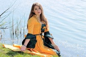 young woman in princess dress sitting by the lake
