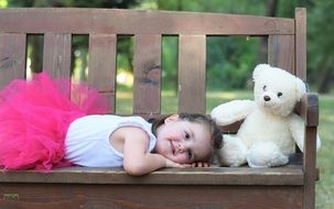 Photo of little girl in a pink skirt on a bench in the park