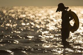 female silhouette in hat standing in water with lifebuoy