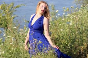 blonde in a blue dress in tall grass near the water